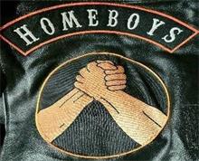 IT CONSISTS OF TWO SEPARATE PATCHES ONE AN UPPER ROCKER PATCH BLACK BACKGROUND ORANGE BORDER WITH THE WORD HOMEBOYS IN ALL CAPITAL WHITE LETTERS USING CARNIVAL FONT IN 2 IN SECOND IS A 9 IN ROUND PATCH BLACK BACKGROUND ORANGE BORDER TWO LEFT HANDS CLAPPED IN A HANDSHAKE FROM THE FOREARMS UP IN FLESH COLOR